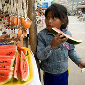 Latin American girl eats watermelon outside a street vendor stall